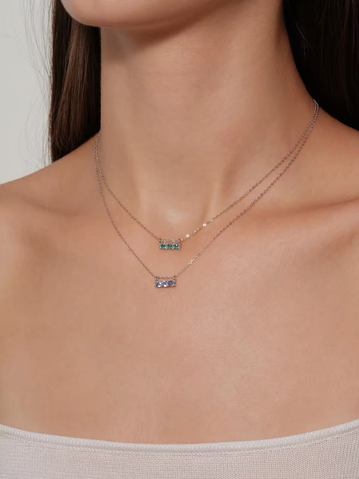 Model wearing layered blue and aqua three-stone necklaces