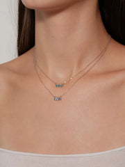 Model wearing layered blue and aqua three-stone necklaces